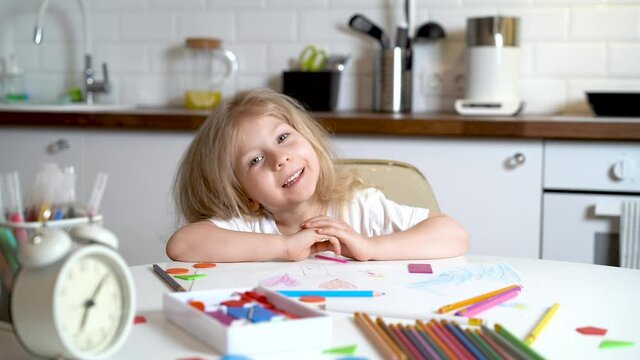 little blonde girl in headphones and with a laptop, sitting at a table in the kitchen and smiling