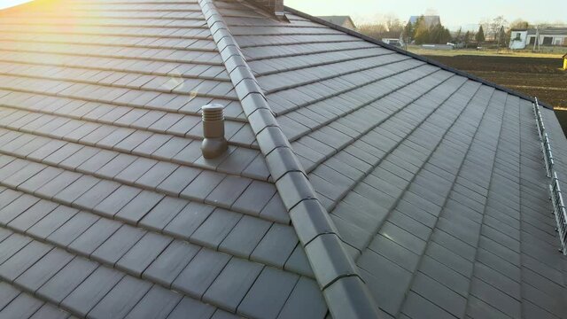 Closeup of ventilation pipe on house roof top covered with ceramic shingles. Tiled covering of building