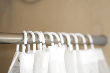 Blurred white plastic hooks curtains for bath. Hooks on an aluminum rod for bathroom curtains. Selective focus