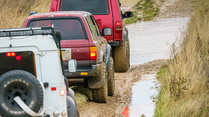 4x4 off-road vehicles driving across mud, water-logged terrain and wading through deep water pools,...