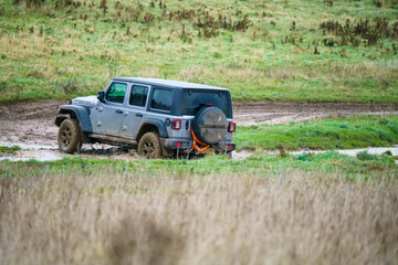 Jeep Rubicon 4x4 off-road vehicle driving across mud, water-logged terrain and wading through deep water pools, Wilts UK. 