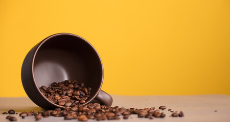 brown cup with coffee and roasted coffee beans, with yellow background