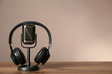Microphone and modern headphones on wooden table against beige background, space for text