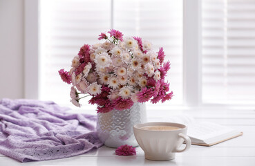 Cup of fresh coffee, open book and beautiful bouquet on white wooden table near window. Good morning