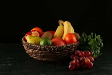 Fresh ripe fruits and wicker bowl on black table