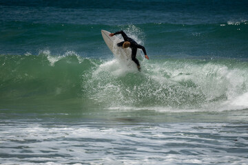 male surfer catching waves surfing at south coast beach on a bright warm sunny day on clear blue water