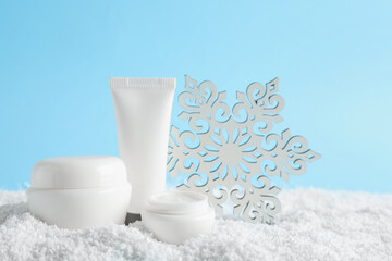 Set of winter skin care cosmetics with hand cream and decorative snowflake on snow against light blue background