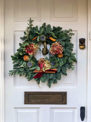 Elegant christmas wreath decorated flowers, orange slices and cinnamon sticks on white wooden door © Alla