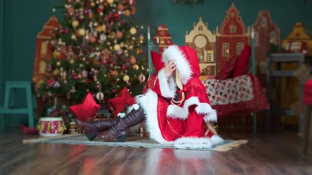 Little Red Riding Hood with gifts. New Year's elf. Sits on the floor, straightens her hair