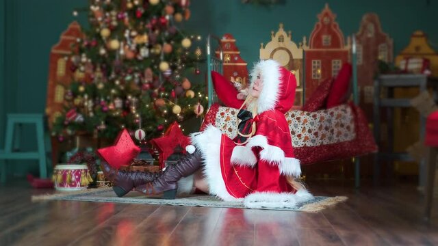 Cute girl cosplaying Christmas Miku Santa dress with gifts. New Year's elf. Sits on the floor, straightens her hair