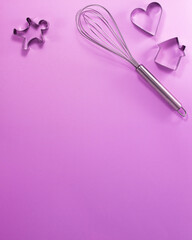 Steel whisk house men and heart shaped cutter flat lay top view. Confectionery cooking concept with copy space on bright purple paper background. National cooking day.