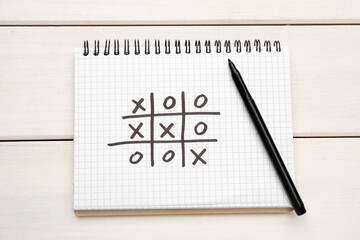 Notebook with tic tac toe game and marker on white wooden table, top view