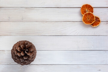 White wooden background with a spruce cone and dry orange slices