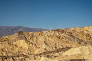 Two Hikers Give Scale To The Golden Shaded Hills Of Death Valley