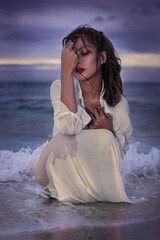 Fototapeta na wymiar pretty young woman kneels in the surf on the seashore
