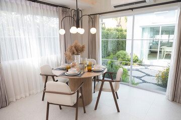 Plate setting on round table in modern style dining room interior of modern home. Dinning room with grass flower and big window.