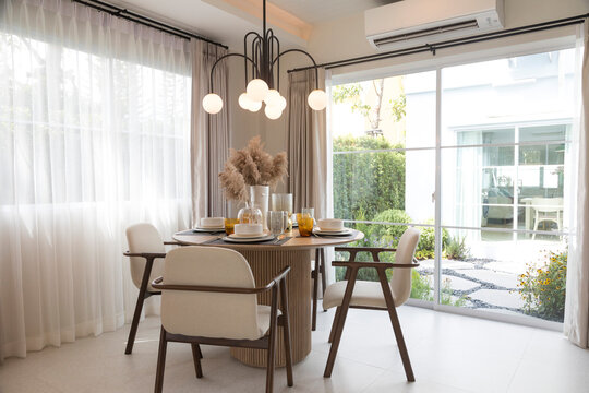 Plate setting on round table in modern style dining room interior of modern home. Dinning room with grass flower and big window.