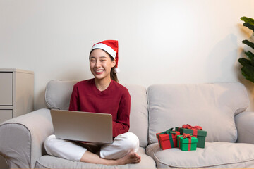 Happy Asian woman make video call on laptop on Christmas day. Celebrating at home with communication technology.