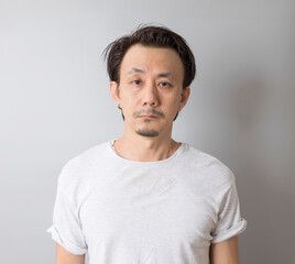 Portrait of self-confident middle age Asian man in a white t-shirt on grey background.
