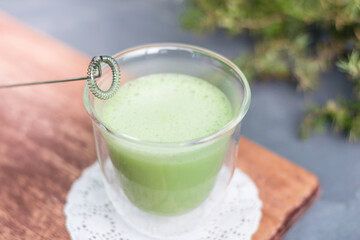 Hot green tea matcha latte with electric whisk. Whipped foam green tea in a glass transparent cup.