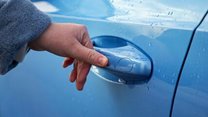 Lady driver in grey warm coat closes automobile door covered with raindrops using sensor fingerprint on autumn day, closeup