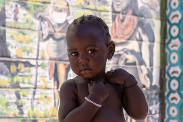 Little african black child stands near a colorful wall on a sunny day