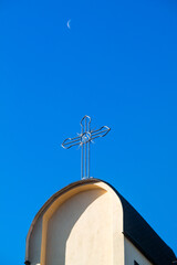 Cross on top of catholic tower church against deep blue sky and morning crescent