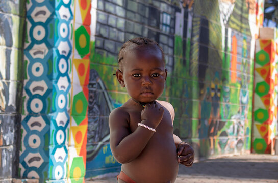 Little african black child stands near a colorful wall on a sunny day. 28.06.2021 Svakopmund. Nmibia