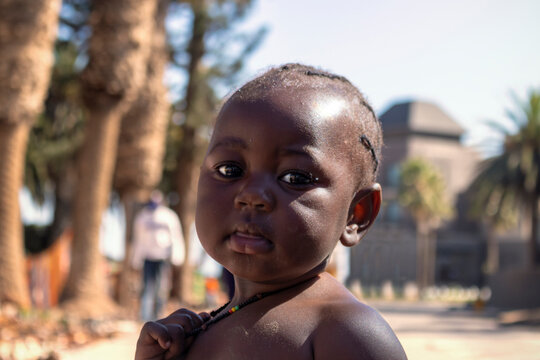Little african black child stands against the blue sky on a sunny day