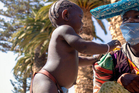 Little african black child and his mother in national clothes stand against the background of palm trees on a sunny day
