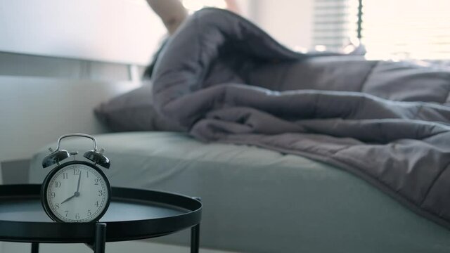 Alarm clock at 8 am in the morning man sleeping wake up press stop alarm and then continued to sleep by covaering his head with a blanket on holiday sunlight shines through the window into the bedroom