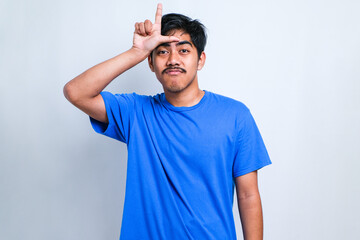 Man wearing casual shirt making fun of people with fingers on forehead doing loser gesture mocking...