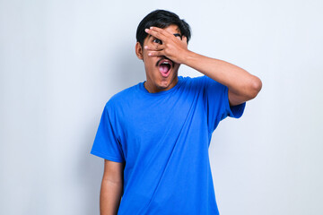 Man peeking in shock covering face and eyes with hand, looking through fingers with embarrassed expression.