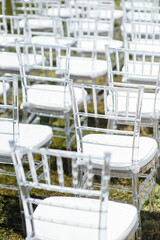 White glass chairs stand on the green grass. Round arch for a wedding ceremony in the background