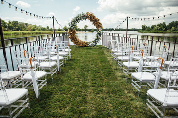 Obraz na płótnie Canvas Round arch for a wedding ceremony by the river. White glass chairs stand for guests