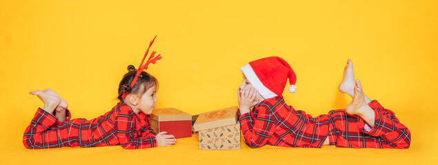 Brother and sister in pajamas lie with gifts on yellow background