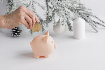 The hand of an elderly Caucasian woman lowers a metal bitcoin coin into a piggy bank pink pig on...