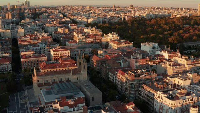 Aerial ascending footage of historic buildings in town illuminated by bright sunset light. Old church and large palaces near El Retiro Park.