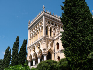 Fototapeta na wymiar Villa Borghese on Isola del Garda Island, a Palace in Venetian Neo-Gothic Style Facade with Palm Trees