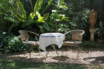 A pair of wicker armchairs and a table with vintage style white tablecloth on a gravel patio area...