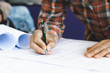 Young technician, engineer, designer holding a pencil drawing on a blueprint on his desk to create a project in the office..And free space to enter your text.