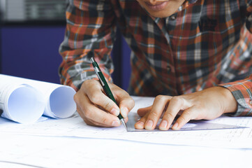 Young technician, engineer, designer holding a pencil drawing on a blueprint on his desk to create a project in the office..And free space to enter your text.