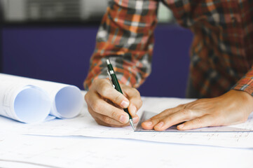 Young technician, engineer, designer holding a pencil drawing on a blueprint on his desk to create a project in the office..And free space to enter your text.