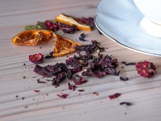 Pink tea from rose petals hibiscus with dried pieces of fruit and berries is scattered on the table by a white tea cup. Tea shop concept