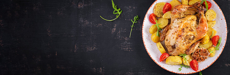Baked chicken with potatoes in a white plate. Dark background. Top view, banner