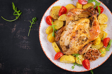 Baked chicken with potatoes in a white plate. Dark background. Top view, copy space.