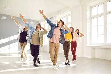 Group of happy young people enjoying a contemporary dance class. Cheerful, talented, beautiful male and female dancers in trendy casual wear dancing together in a modern, light, sunny dance studio