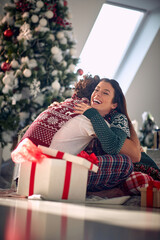 Obraz na płótnie Canvas A young couple in love is in a hug while sitting on the floor at home and sharing christmas presents. Christmas, home, relationship, presents