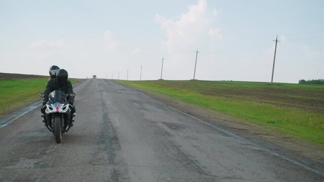 Empty rural road between spring fields and couple enjoying motoriding at picturesque countryside under sky with white clouds slow motion