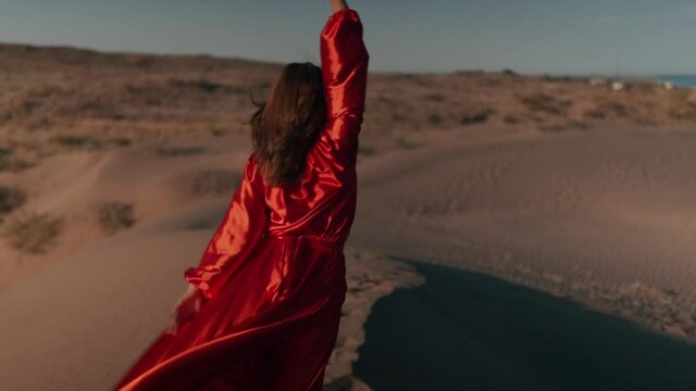 An Asian woman in a red dress dancing on sand dunes